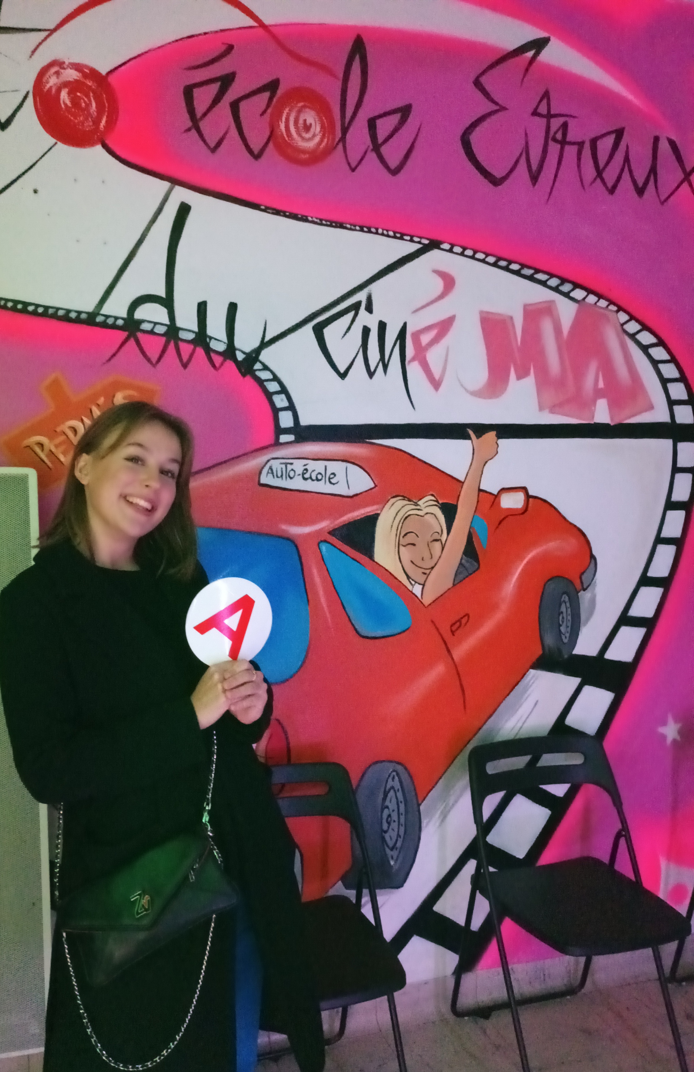 Élève souriante devant la fresque Auto École du Ciné